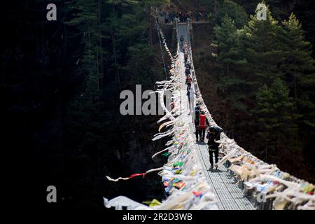 Trekkers pass over one of many swinging bridges in the Everest Region. Stock Photo