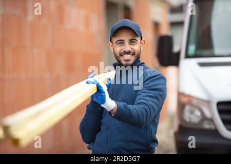 young carpenter carrying wood on shoulder at construction site Stock Photo