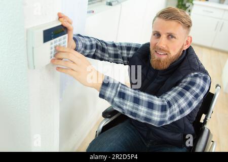 disabled male electrician installing security system door sensor on wall Stock Photo
