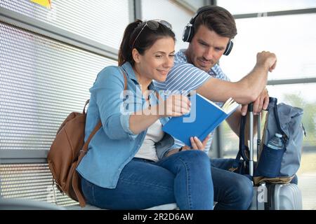 couple sitting at train station checking a book while waiting Stock Photo