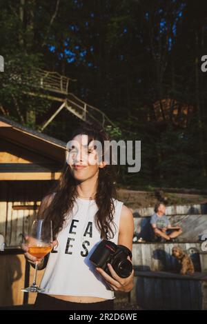 natural woman smiles with beverage and camera in afternoon sun Stock Photo