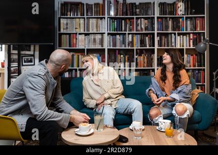 Three friends from college, owners of a small bookstore and library, happy because they opened their own library with rare professional books that the Stock Photo