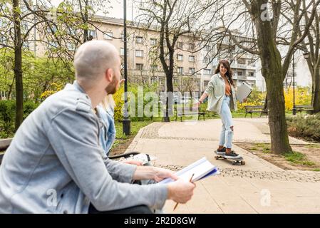 Young business people are sitting in the park on a bench having a staff meeting looking for premises or an apartment for rent to move their small comp Stock Photo