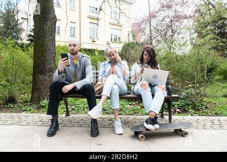 Young business people are sitting in the park on a bench having a staff meeting looking for premises or an apartment for rent to move their small comp Stock Photo