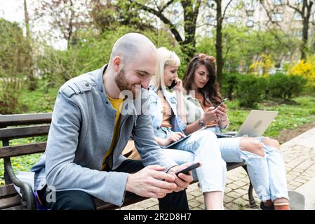Young business people are sitting in the park on a bench having a staff meeting looking for premises or an apartment for rent to move their small comp Stock Photo