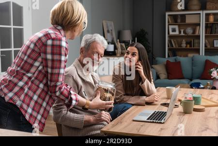 Beautiful happy family together at the table father mother daughter while father works on laptop daughter helps him. Senior couple have granddaughter Stock Photo