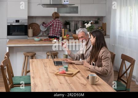 Senior couple and daughter at laptop learns internet communication. Daughter teaching father to use laptop computer for surfing the net and online pay Stock Photo