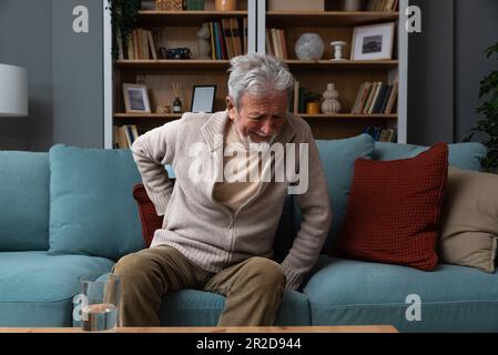 Aged grey haired senior red face man writhes in pain suffers from low back strain, touch rubbing or massaging loin reduces backache. Degenerative disk Stock Photo