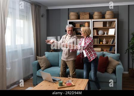 Joyful active old retired romantic couple dancing laughing in living room, happy middle aged wife and elder husband having fun at home, smiling senior Stock Photo