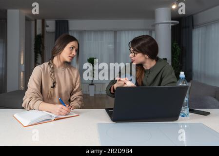 Two Happy Ladies Using Laptop Computer Working And Learning Online Together Or Making Video Call Sitting At Desk In Modern home Office. E-Learning. Fe Stock Photo