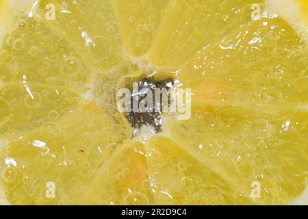 Close-up of a lemon slice in liquid with bubbles. Slice of ripe lemon in water. Close-up of fresh citron slice covered by bubbles. Macro horizontal Stock Photo