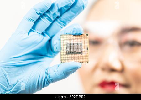 A female engineer working in a lab wearing protective goggles and gloves holds the new processor in her hands and examines it. Scientist holding chips Stock Photo