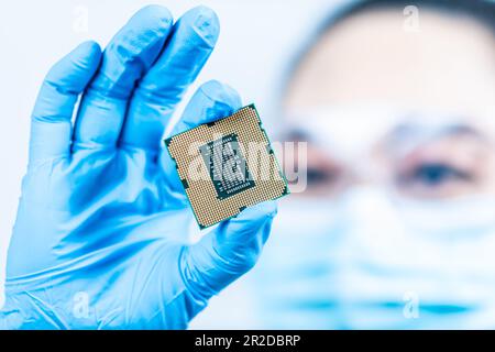 A female engineer working in a lab wearing protective goggles and gloves holds the new processor in her hands and examines it. Scientist holding chips Stock Photo
