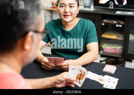 Couples playing cards at home for date night inside. They both held cards in their hands and smiled happily. Concept for game on, looking at camera, e Stock Photo