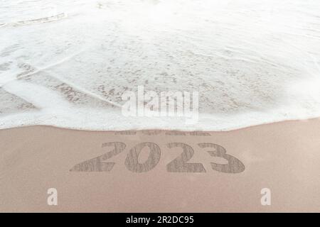change new year of 2023 on sand of beach. New Year 2023 Concept. inscription is a 2023 number on sand beach. Sandy beach and sea wave beautiful backgr Stock Photo