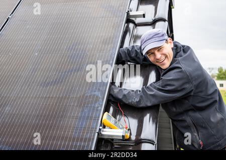 Smiling technician working on the installation of a solar panel on a roof Stock Photo