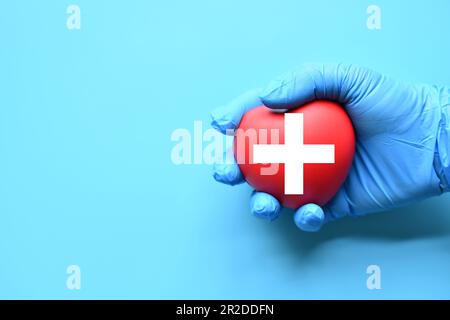 A red cross is a symbol of medical health. Hand holding a heart and on a blue background. Copy space for the text and contents. red cross CPR, World h Stock Photo