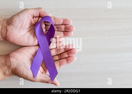 International Overdose Awareness Day, hand holds purple awareness ribbon on wooden table, a concept for World Lupus Day, Autoimmune disease, Immune Sy Stock Photo
