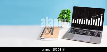 Laptop screen shows a graph of the 2023 economy rising and is placed on wooden desk in office. Business growth concept. technology work notebook compu Stock Photo