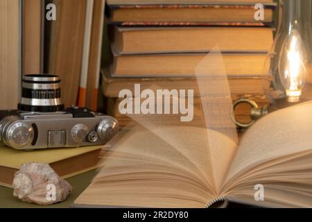 An open old book, the pages of which are in motion from turning the pages. On the table there are also a lot of old books and an analog camera. Stock Photo