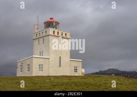 View from the coast on the lighthouse. Intense rainy clouds in the autumn. Mountain in the background. Green grass. Dyrholaey, Iceland. Stock Photo