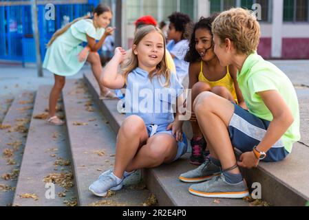 Happy tweenagers friends sitting on steps outdoors and chatting Stock Photo