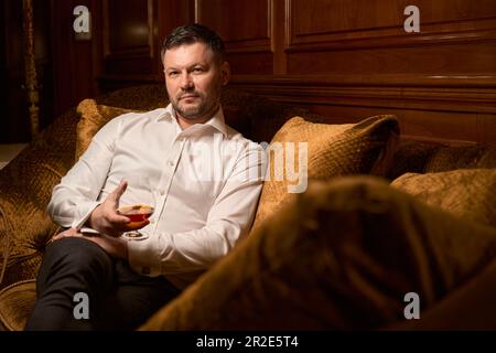 Male guest drinking expensive brandy on luxury sofa in the restaurant Stock Photo