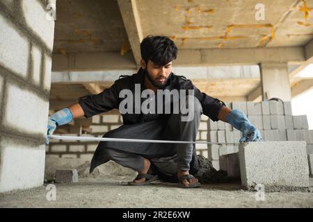 construction worker levels or measures a cement brick wall using measuring tape Stock Photo