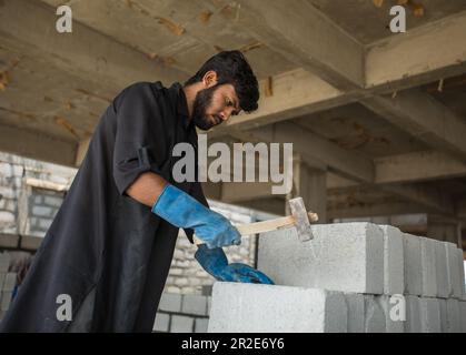 A construction labor worker broking a concrete brick using a hammer Stock Photo