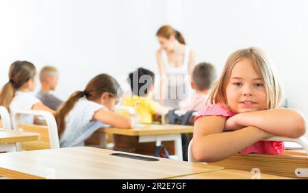 Cheerful tween schoolgirl sitting at school desk at lesson Stock Photo ...