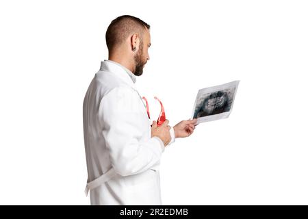 Bearded man, doctor in white med gown looking at x-ray scan checking health condition against white background Stock Photo