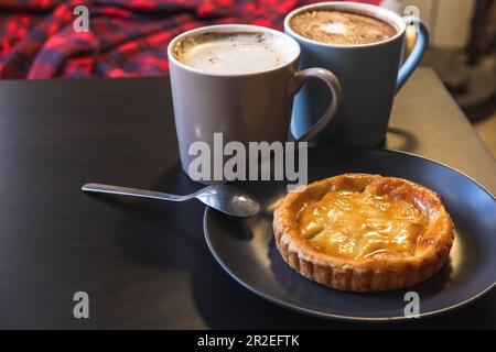 Pastel de nata, Portuguese egg custard tart pastry is on black table near two cup of cappuccino coffee Stock Photo