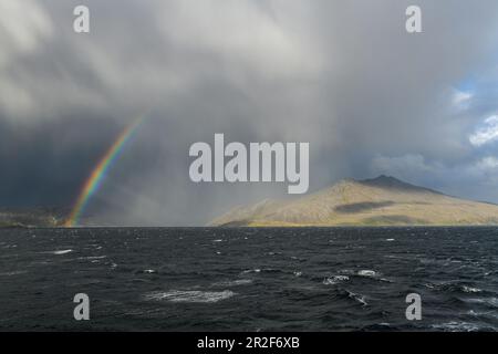 A rainbow forms between thick clouds drifting over low mountains, Chilean fjords, Magallanes y de la Antartica Chilena, Patagonia, Chile, South Americ Stock Photo