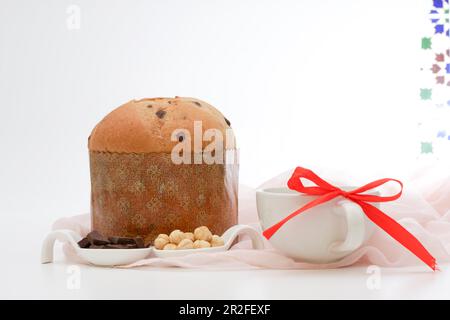 Panetone on a pink cloth ceramic spoons with hazelnuts and chocolate and white mug with a red ribbon Stock Photo