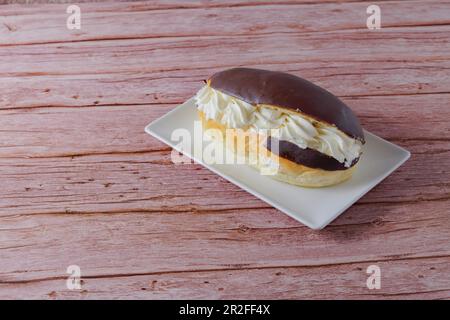 Chocolate-covered cream eclair on a white plate on a wooden table Stock Photo