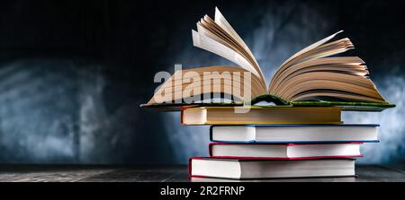 A composition with an open book lying on a stack of other books Stock Photo