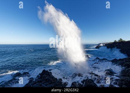 The surf crashes through lava tubes upwards. A prompter on the coastal road south of St-Leu. Stock Photo