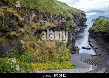 Looking down into small port of Gjogv. Stairs in the foreground, fishing boat. Eysturoy, Faroe Islands. Stock Photo