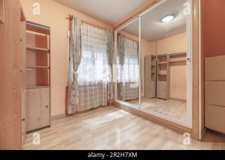 A room with a built-in wardrobe with sliding mirror doors and white aluminum edges Stock Photo