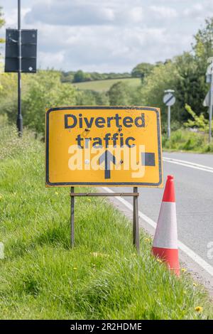 UK road transport system. Orange and white road cone & diverted traffic sign on country road grass verge in sunshine. For roadworks, traffic diversion Stock Photo