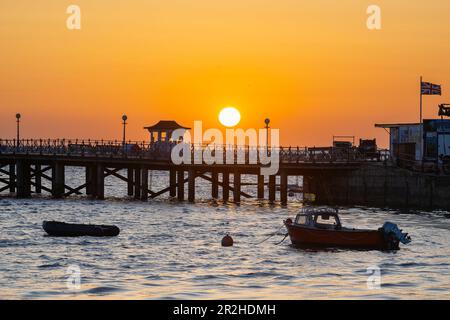 The sky glows orange during the sunrise above the pier at Swanage in Dorset. Stock Photo