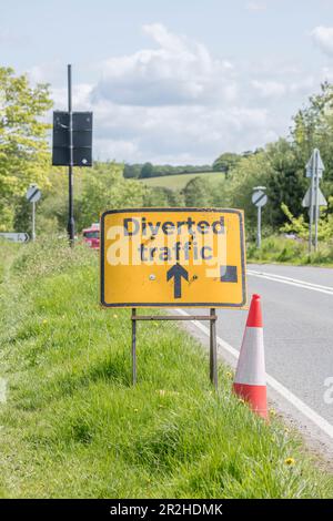 UK road transport system. Orange and white road cone & diverted traffic sign on country road grass verge in sunshine. For roadworks, traffic diversion Stock Photo