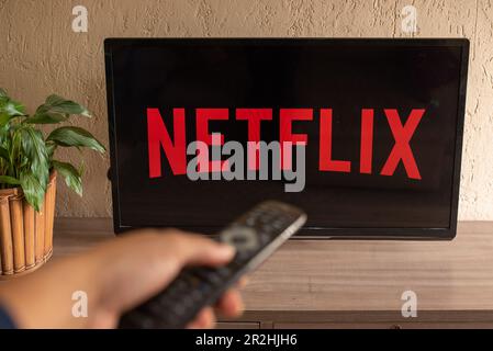 Brazil, Rio de Janeiro - May 19, 2023: TV Television Netflix logo on screen with home remote control. Stock Photo