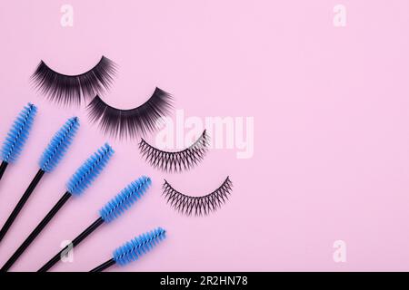 Fake eyelashes and brushes on pink background, flat lay. Space for text Stock Photo