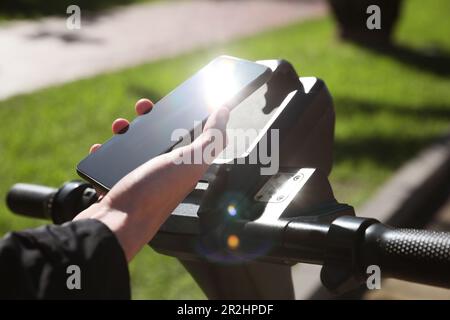 Man using smartphone to pay and unblock rental electric scooter outdoors, closeup Stock Photo