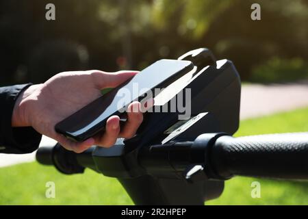 Man using smartphone to pay and unblock rental electric scooter outdoors, closeup Stock Photo