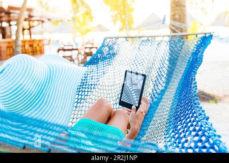 Woman reading from Kindle tablet lying on hammock, Zanzibar, Tanzania, East Africa, Africa Stock Photo
