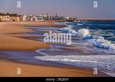 The beach with crashing waves at the jetty in Swakopmund in Namibian Africa at sunset Stock Photo