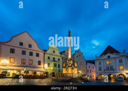 Fountain and Plague Column and traditional houses with gables in background at twilight, Namesti Svornosti Square in historical center, UNESCO Stock Photo