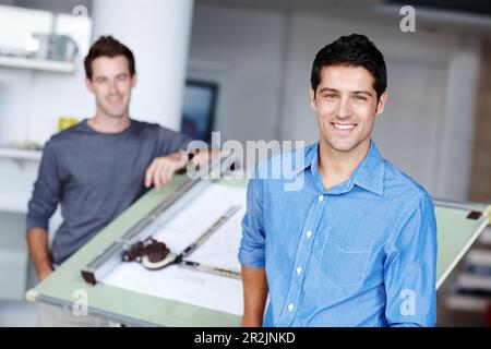 Proud of his designs. Two young architects standing beside an easel with their blueprint on it. Stock Photo